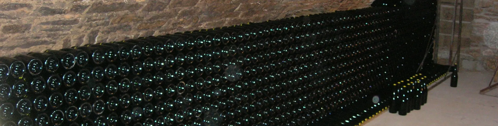 Bouteilles empilées sur lattes dans une cave voûtée en pierre